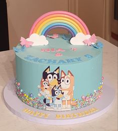 a birthday cake decorated with cartoon characters and a rainbow in the background on a table