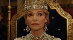 an older woman wearing a tiara and pearls in front of a golden throne with candles