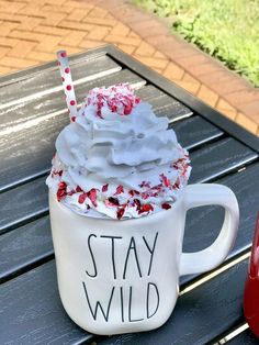 a cup with whipped cream and sprinkles sits on a picnic table next to a red fire hydrant