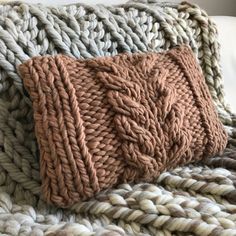 a knitted pillow on top of a white couch next to a brown and beige blanket