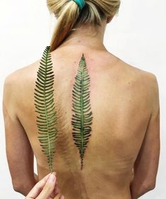 a woman with a tattoo on her back has a fern leaf tattooed on her upper back