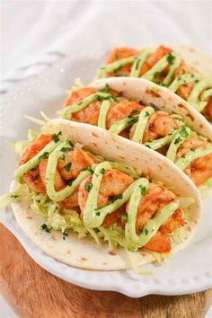 three shrimp tacos with avocado sauce on a white plate