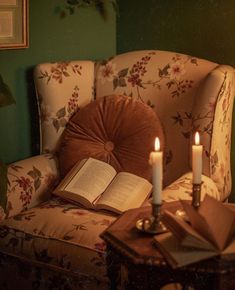 an open book sitting on top of a chair next to two lit candles