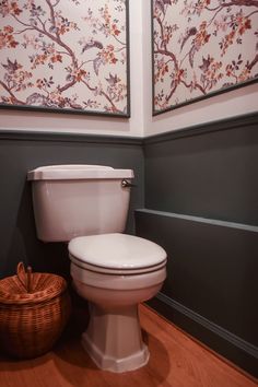 a white toilet sitting in a bathroom next to a basket and painting on the wall