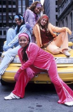 the group of young women are posing on top of a yellow car in the street