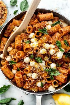 a skillet filled with pasta, cheese and spinach sprinkled with basil