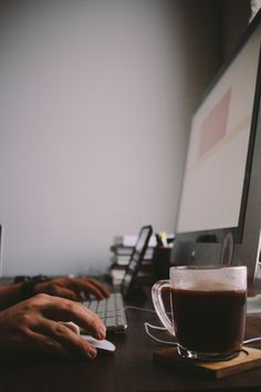 a person typing on a computer with a cup of coffee in front of them,