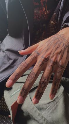 a person's hand with tattoos on it sitting in front of a bag and wearing a jacket