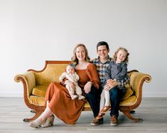 a family sitting on a couch in front of a white wall and wood flooring