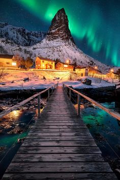 a wooden walkway leading to a cabin under the aurora lights in norway with mountains and snow covered ground