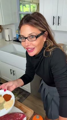 a woman in black shirt and glasses preparing food on cutting board next to counter with utensils