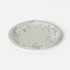 a white and green plate with flowers on the rim, sitting against a white background