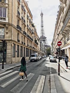 a woman is crossing the street in front of some tall buildings with cars parked on both sides