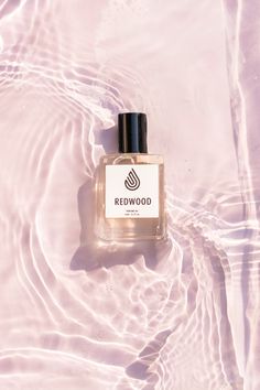 a bottle of redwood cologne sitting on top of a pink surface next to water