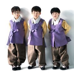 three young boys dressed in purple and yellow outfits, standing next to each other against a white wall