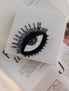 an eye brooch sitting on top of a book with black and white pins sticking out of it