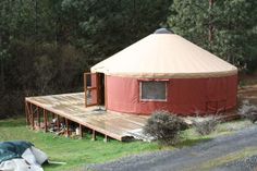 a red yurt sitting on top of a lush green field next to a forest