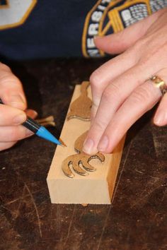 a person is carving letters on a piece of wood with a small blue pen in their hand