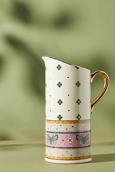 a white and gold coffee cup sitting on top of a table next to a green wall