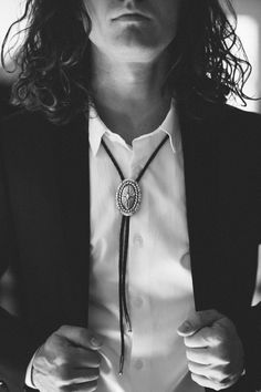 a man with long hair wearing a white shirt and black blazer