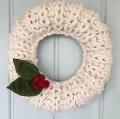 a knitted wreath hanging on the front door with two red berries and green leaves