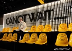 a woman sitting in front of yellow chairs with smiley faces painted on the wall behind them