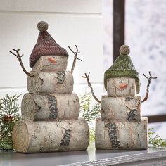 two snowmen made out of logs sitting on top of a table next to each other