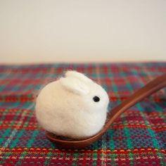 a small white bird sitting on top of a wooden spoon filled with wool and yarn