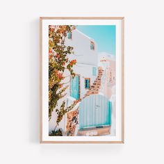 a framed photograph of a white house with blue shutters and flowers on the outside