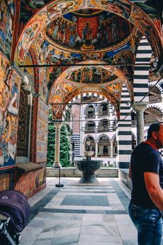 a man walking down a walkway next to a building with paintings on the walls and ceiling