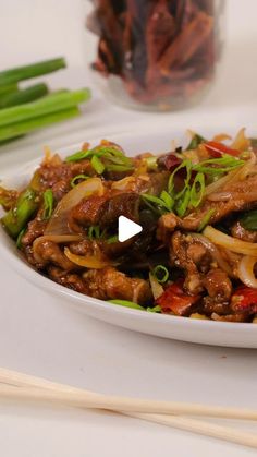 a white plate topped with meat and veggies next to chopsticks on a table