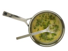 a pot filled with broccoli soup on top of a white table next to a spoon