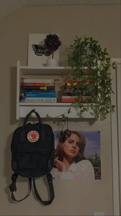 a black backpack hanging on the wall next to a book shelf with books and plants