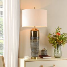 a table lamp sitting on top of a dresser next to a vase filled with flowers