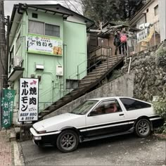 a white car parked in front of a green building with stairs leading up to it