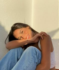 a beautiful young woman sitting on top of a wooden floor next to a white wall