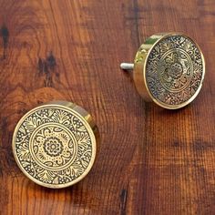 two brass knobs on a wooden surface with an intricate design inlayed to them