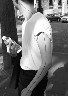 a young man standing next to a tree on a sidewalk holding a bottle of water