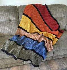 a couch with a multicolored blanket sitting on it's back next to a pillow