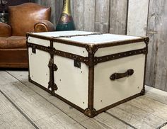 an old trunk is sitting on the floor next to a leather chair and champagne bottle