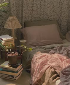 a bed with pink sheets and pillows next to a table with books on top of it