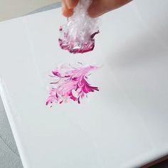 a person is holding something in their hand while they are painting flowers on a piece of paper