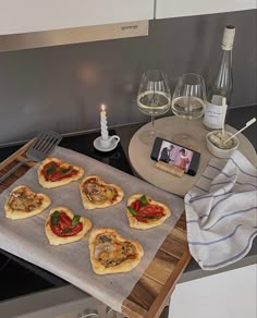 small pizzas sitting on top of a baking sheet next to wine glasses and a cell phone