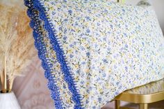 a crocheted blue and yellow blanket sitting on top of a bed next to a vase