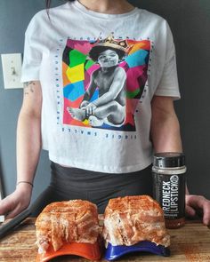 a woman standing in front of two sandwiches on a cutting board next to a can of soda