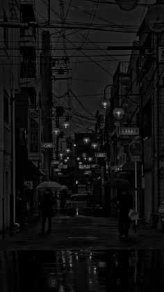 black and white photograph of people walking down the street at night with umbrellas in hand