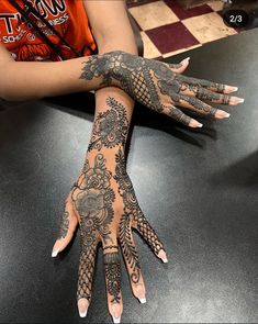 a woman's hands with hennap and tattoos on her arm, sitting at a table