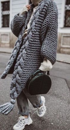 a woman is walking down the street with her hand on her hip, wearing a gray coat and white sneakers