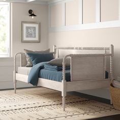 a white bed with blue pillows in a room next to a window and rug on the floor