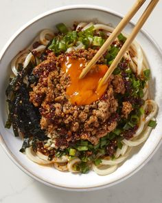 a bowl filled with noodles, meat and veggies next to chopsticks